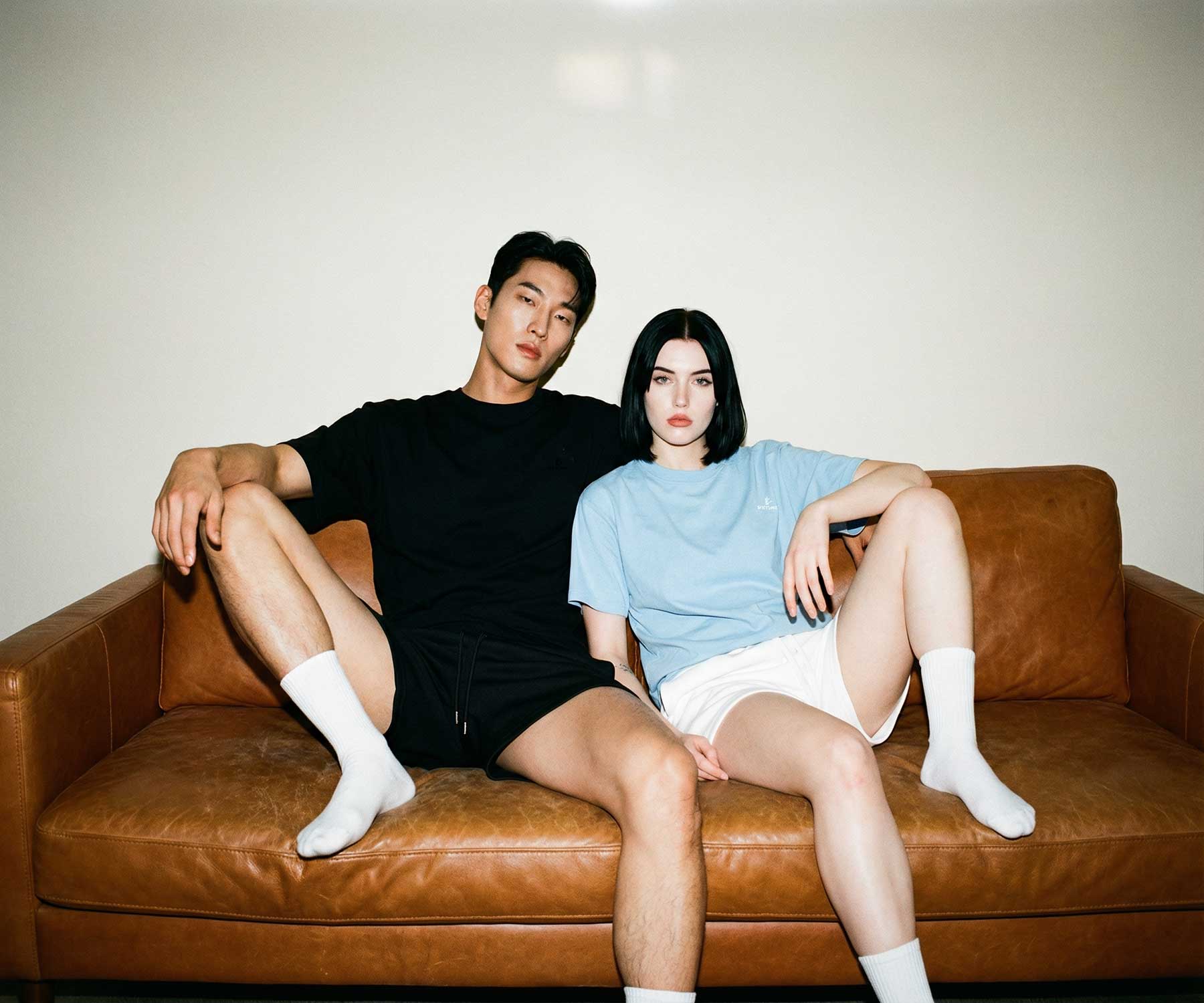 Two people sitting on a brown leather couch against a plain wall.