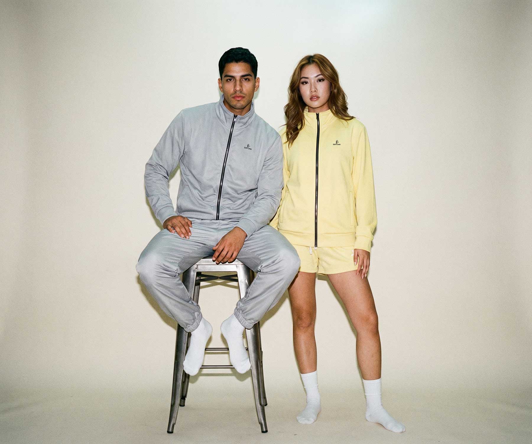 Two people wearing matching tracksuits on a plain background