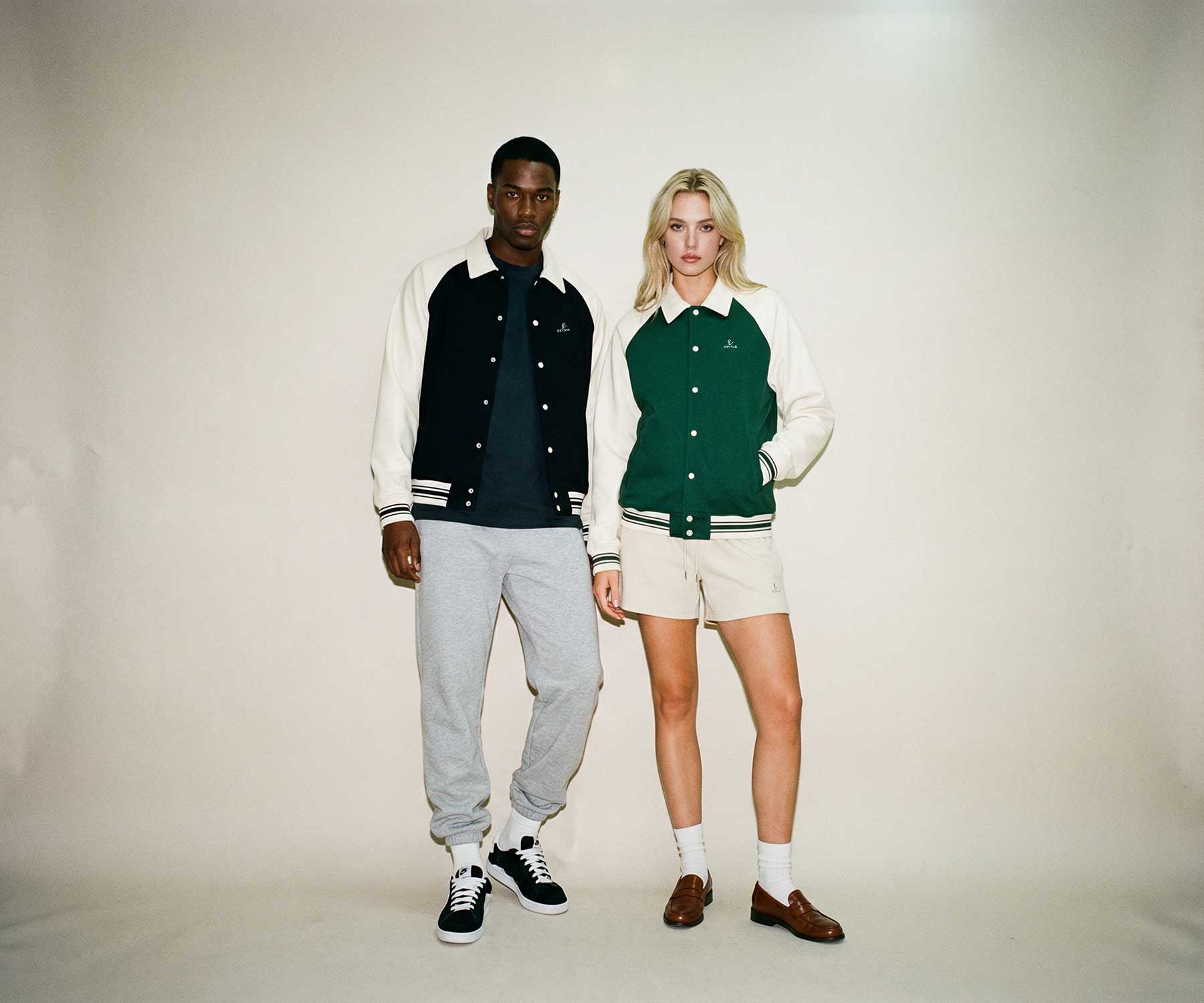 Two people wearing letterman jackets standing against a plain background