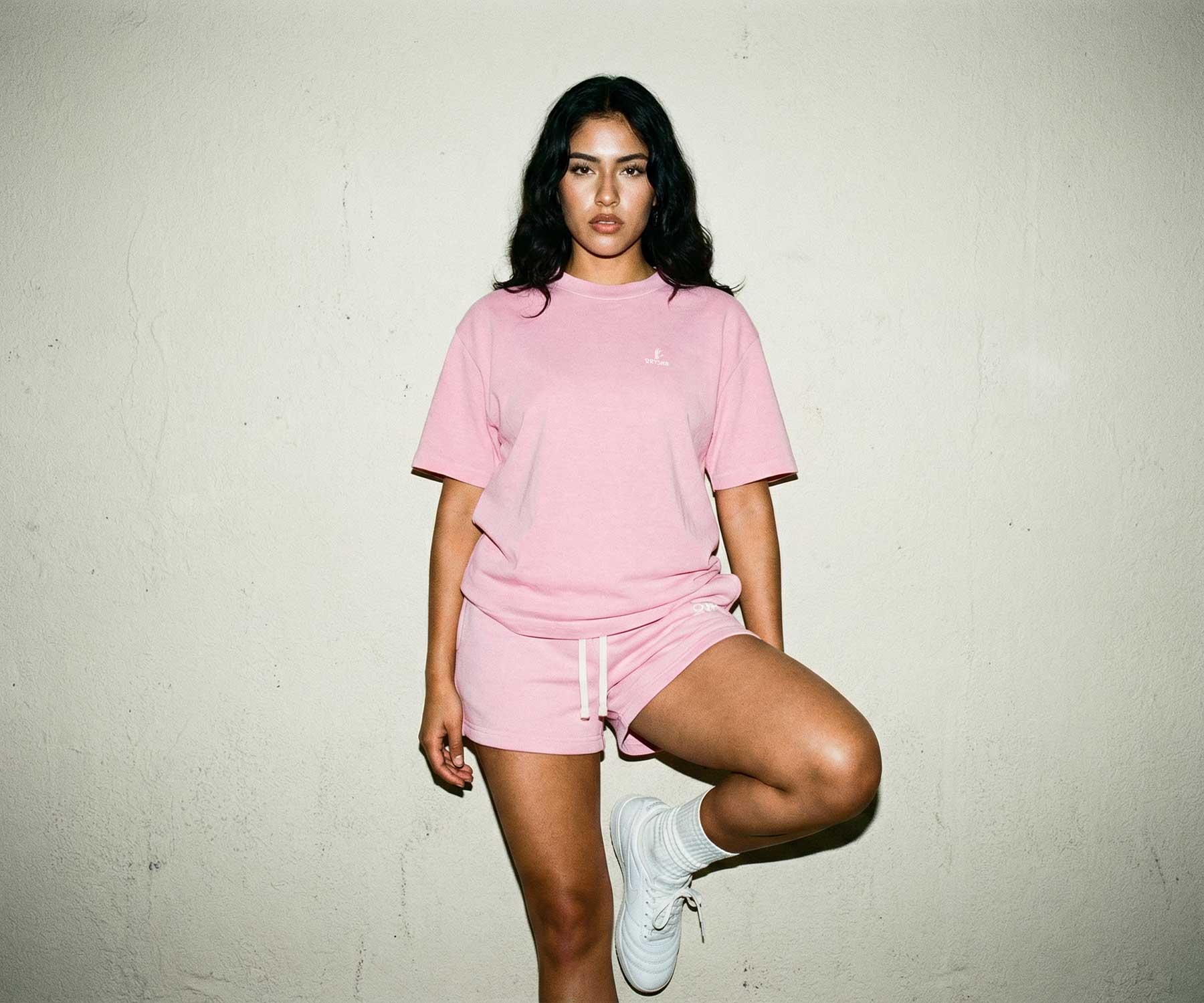 Woman wearing a pink outfit with a logo against a plain background
