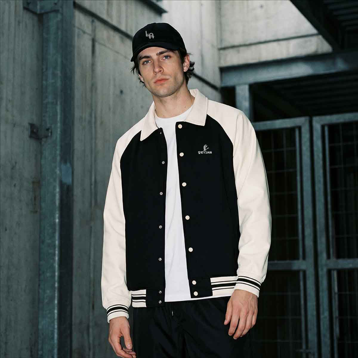 Man wearing a black and white varsity jacket with a cap in an urban setting